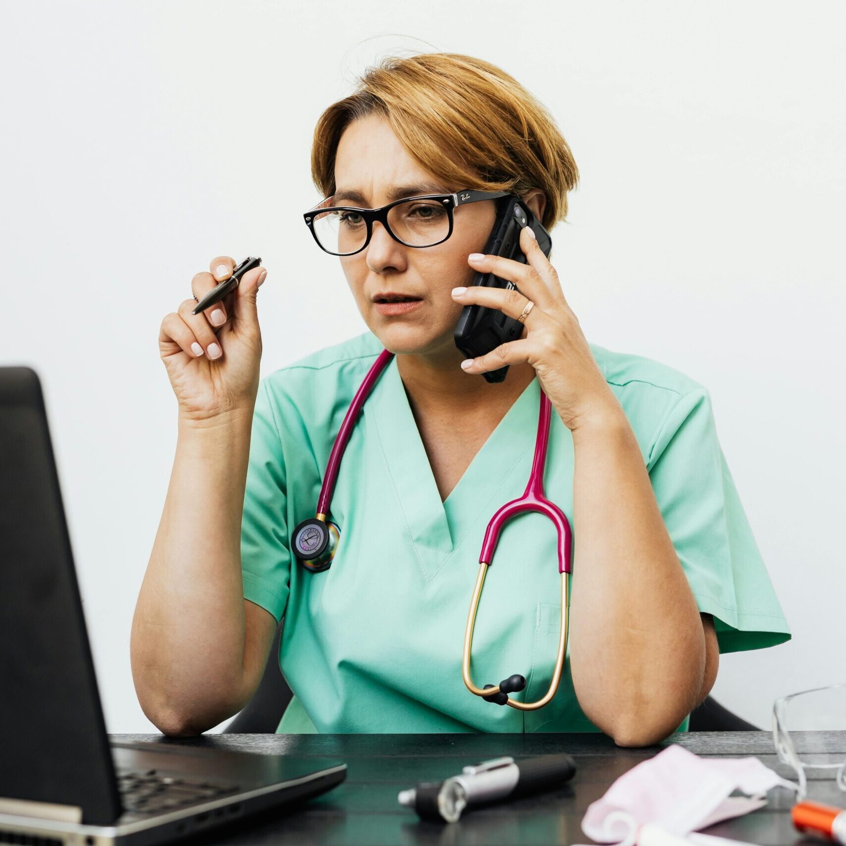Female doctor with a pink stethoscope at a laptop answers a call and takes notes.