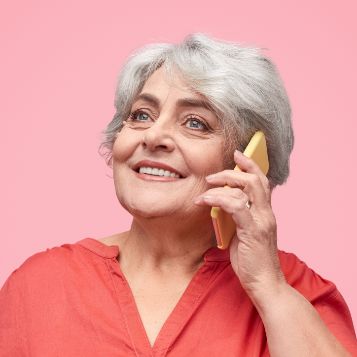 Elderly woman with gray hair smiles while talking on a yellow telephone