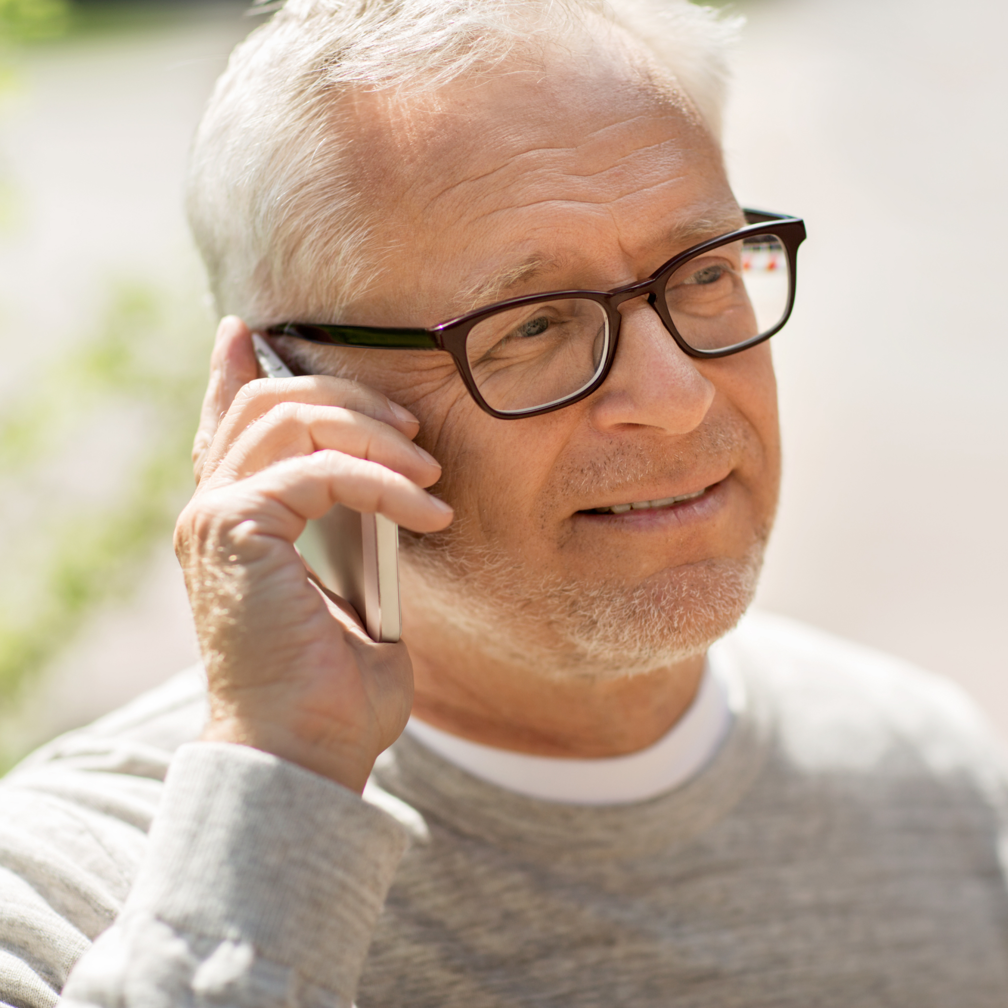 Elderly man in gray shirt talking through a phone